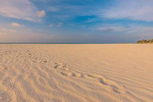 strand bakgrund med fotspår i sand närbild. begrepp för resa semester. inspirera avkopplande strand, Vinka och fotspår på solnedgång tid. mjuk pastell blå himmel, hav se horisont. äventyr scen foto