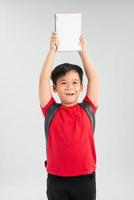 ung asiatisk pojke studerande innehav bok och visa över huvud, isolerat på vit bakgrund foto