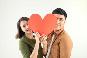 Lycklig ung asiatisk par innehav hjärta form över vit bakgrund. foto