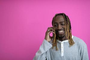 afro kille användningar en telefon medan Framställ i främre av en rosa bakgrund. foto