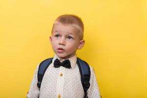 tillbaka till skola. en blond pojke med en ryggsäck i en ljus skjorta på en gul bakgrund utseende upp. kopia Plats. utbildning. baner foto