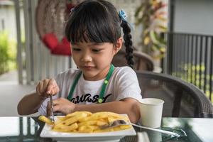 ung asiatisk flicka äter franska frites ung unge roligt Lycklig potatis snabb mat. foto