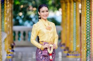 attraktiv thailändsk kvinna i en uråldrig thailändsk klänning håller en fräsch krans och hyllar Buddha för att önska sig den traditionella songkran-festivalen i thailand foto