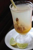 ett glas varm ingefärsdryck och lime. dekorerad med citrongräs i glaset. klar. läggs på en kastrull plus en tunn skiva lime foto