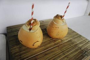 två kokosjuicer med papperssugrör placerade på ett träbord foto