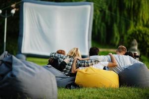 ung multietnisk grupp människor som tittar på film på poff i utomhusbio. foto
