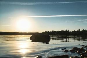 sjö i Sverige, smalland på solnedgång med sten i förgrund av vatten med skog foto