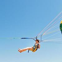 flicka parasailing på fallskärm i blå himmel foto