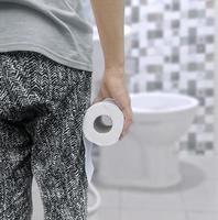 en person lidande från diarre innehar en rulla av toalett papper i främre av de toalett skål foto