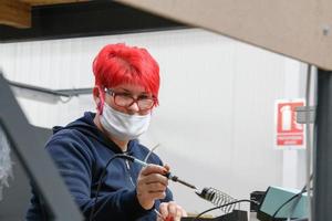 industriell arbetstagare bär en ansikte mask på grund av till en coronavirus pandemi lödningar kablar från fabrik produktion Utrustning foto