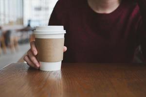 kvinna hand innehav vit papper kopp av varm kaffe i kaffe Kafé. foto