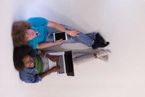 multietnisk par Sammanträde på de golv med en bärbar dator och läsplatta topp se foto