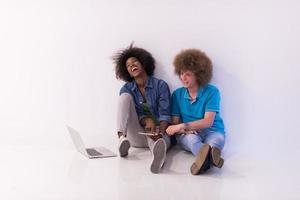 multietnisk par Sammanträde på de golv med en bärbar dator och läsplatta foto
