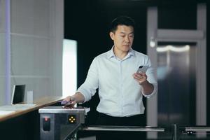 framgångsrik asiatisk affärsman arbetstagare går in kontor, användningar nyckel kort till öppen vändkors foto