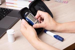 kvinna händer med en glukometer på de skrivbord. de livsstil av en person med diabetes, mätning de nivå av glukos i de blod foto