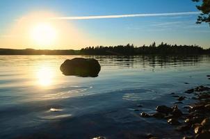 sjö i Sverige, smalland på solnedgång med sten i förgrund av vatten med skog foto