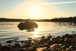 sjö i Sverige, smalland på solnedgång med sten i förgrund av vatten med skog foto