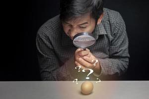 en man innehav en förstorande glas gester med en förstorande glas, ser i häpnad på de ägg liggande på de tabell och de tömma Plats. foto