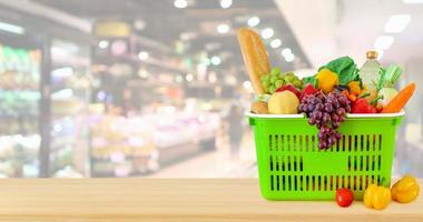 varukorg fylld med frukt och grönsaker på träbord med supermarket livsmedelsbutik suddig oskarp bakgrund med bokeh ljus foto