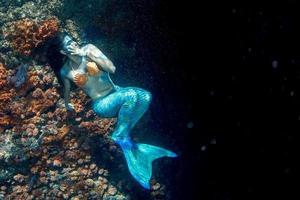 skön sjöjungfru simning under vattnet i de djup blå hav foto
