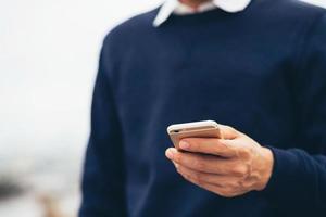 ung man bär rutig skjorta. närbild hand med på mobiltelefon under vila på soffan. sitter och tittar på meddelandet på mobiltelefonen under pausen, slappna av. mjukt fokus. foto