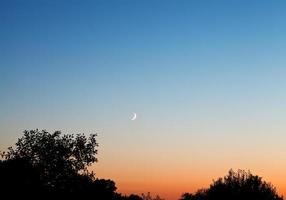 ny måne i mörk blå himmel på solnedgång foto