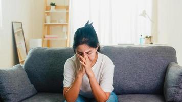 asiatisk affärskvinna stressad med huvudvärk som sitter på soffan i vardagsrummet foto