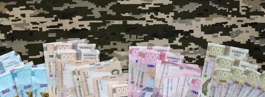 ukrainska hryvnya räkningar på tyg med textur av ukrainska militär pixeled kamouflage. trasa med camo mönster i grå, brun och grön pixel former foto