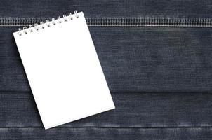 vit anteckningsbok med rena sidor liggande på mörk blå jeans bakgrund. bild med kopia Plats foto