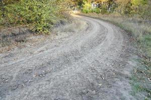 höst landskap med en böjd väg och spår av de trampa av stor hjul av jordbruks maskineri foto