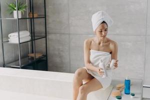 kvinna applicering fuktgivande hudvård kosmetika för kropp hud efter tar en dusch i badrum foto