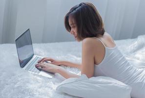 asiatisk kvinna som arbetar på en bärbar dator på sängen foto