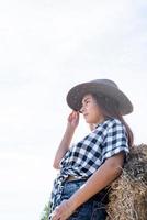 skön kvinna i pläd skjorta och cowboy hatt vilar på höstack foto
