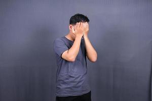 deprimerad asiatisk ung man har stressig tid med händer beläggning ansikte. isolerat på grå bakgrund. foto