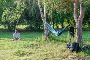 stilig europeisk man Sammanträde på en gräs i sommar parkera nära till hängmatta med hund, med elektrisk skoter. foto