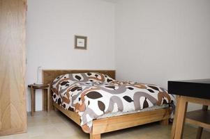 säng bas, sovrum med matta på de golv, lera pott i de bakgrund, trä- credenza och spegel. foto