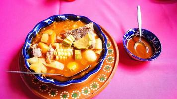 lera tallrik med pozole, traditionell mexikansk mat, rosa bordsduk, metall sked foto