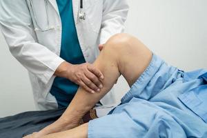 asiatisk läkare fysioterapeut undersöker, masserar och behandlar knä och ben hos senior patient på ortopedmedicinsk klinik sjuksköterska sjukhus. foto
