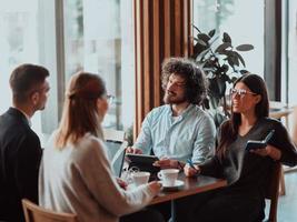 en grupp av ung entreprenörer på en kaffe ha sönder diskutera de projekt medan använder sig av modern redigering tabletter, en smartphone och en laptop.business begrepp foto