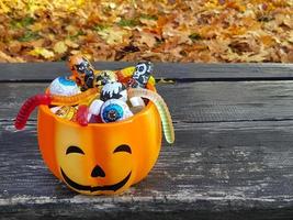 halloween orange pumpa domkraft o lykta pott full av blandad godis - traditionell choklad och gelé maskar. utomhus höst bakgrund med kopia Plats på trä- bänk. lura eller behandla begrepp. foto