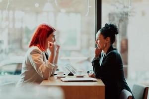 två ung företag kvinnor Sammanträde på tabell i cafe.girl använder sig av bärbar dator, smartphone, bloggar. lagarbete, företag möte. frilansare arbetssätt... foto