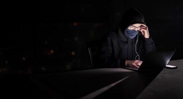 hacker använder sig av bärbar dator dator medan arbetssätt i mörk kontor foto