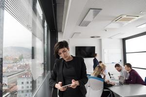 elegant kvinna använder sig av mobil telefon förbi fönster i kontor byggnad foto