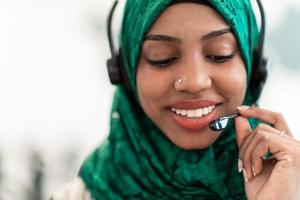 afro muslim kvinna med grön hijab scarf kund representativ företag kvinna med telefon headsetet portion och stödjande uppkopplad med kund i modern ring upp Centrum foto