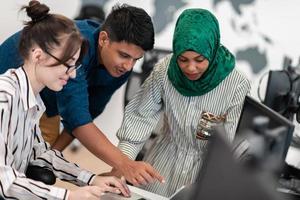 multietnisk börja företag team arab kvinna bär en hijab på möte i modern öppen planen kontor interiör brainstorming, arbetssätt på bärbar dator och skrivbordet dator. selektiv fokus foto