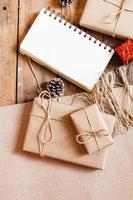 jul gåva låda använda sig av brun återvunnet papper och en anteckningsbok och tall koner på en trä- tabell. foto