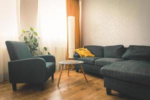 mysigt lägenhet levande rum med soffa och gul kuddar och stilisg tabell med bok förbi blomma och fönster med blå ljus utanför i vinter. grå fåtölj .opy klistra vägg bakgrund foto