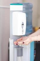 stänga upp av kvinnas hand använder sig av automatisk alkohol dispenser för rengöring hand i de sjukhus. infektion förebyggande begrepp. spara och rena i offentlig medicinsk Centrum område. foto