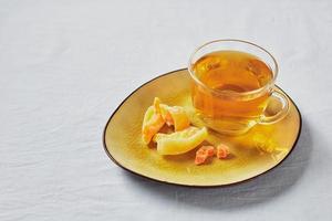 utsökt svart te i glas kopp och kanderad frukt på gul fat foto