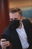 företag man använder sig av smart telefon på lyx kontor bär ansikte mask foto